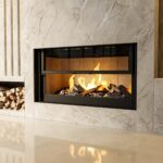 MF Evo Fire 02 Lareira contemporânea embutida em parede de mármore, com chamas visíveis e pilha de lenha ao lado esquerdo.